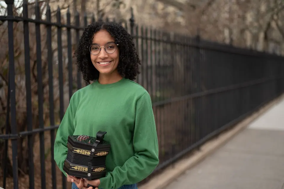 Zohra Coday in a green sweater holding her concertina